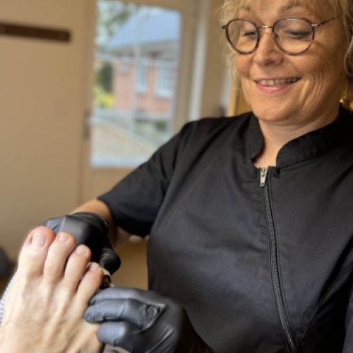 Professionel fodpleje udført af behandler iført sorte handsker på en klinik